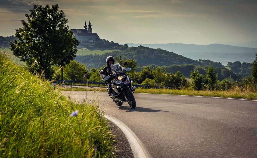 Wohlfühlhotel Rockenschaub **** © Moppetfoto.de Motorradfahrer auf einer kurvigen Straße vor grünen Hügeln und einer Kirche