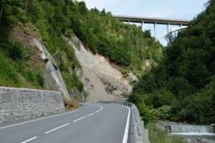 Kurvige Bergstraße mit Hangrutsch und Brücke im Hintergrund