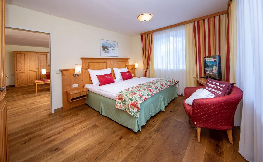 Gemütliches Hotelzimmer mit Doppelbett, Holzmöbeln und rotem Sessel