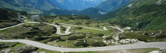 Kurvenreiche Bergstraße mit Schneebedeckten Gipfeln und grünem Tal