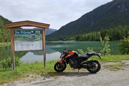 Motorcycle by a lake with a trail map and mountains in the background