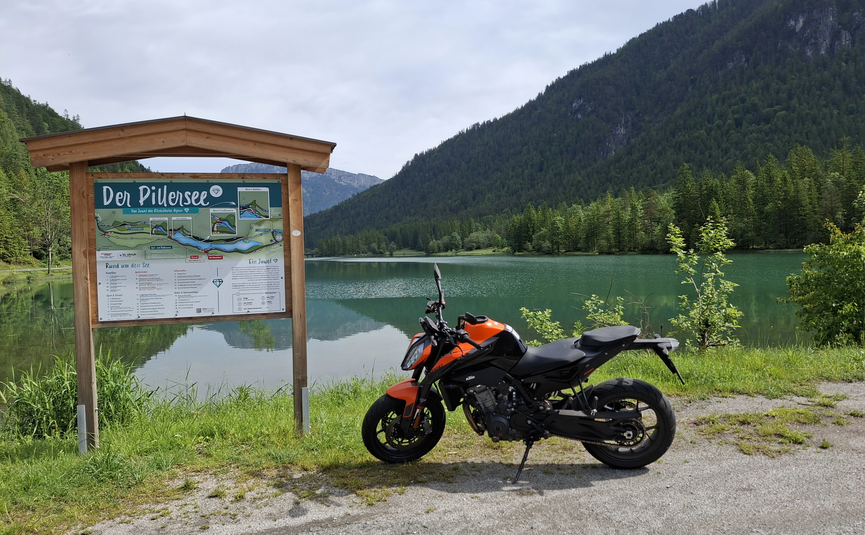 Motorrad neben einem See mit Wanderkarte und Bergen im Hintergrund