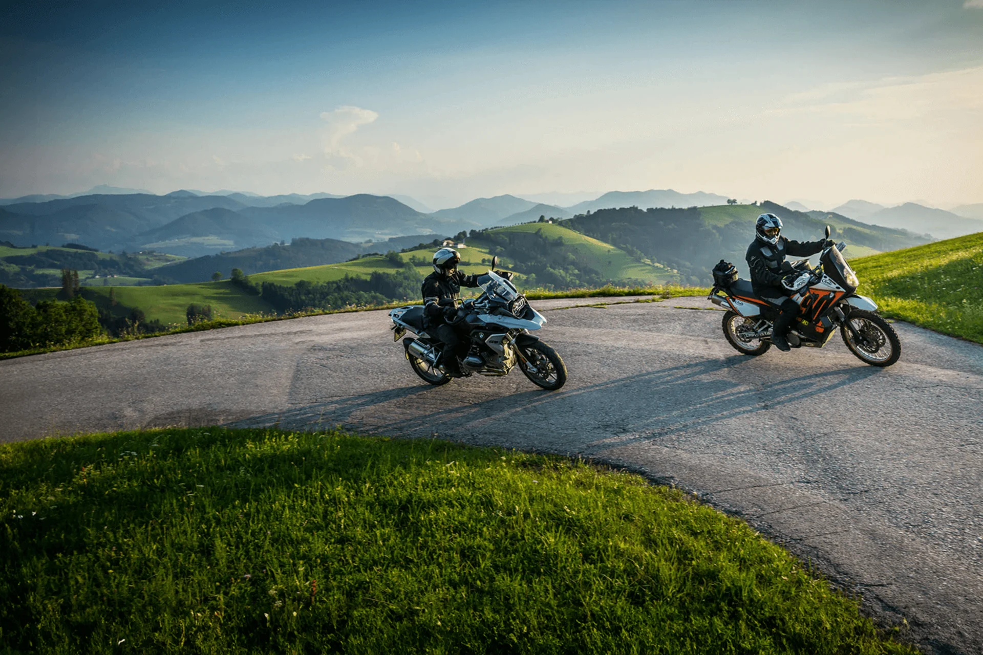 Zwei Motorradfahrer auf kurviger Bergstraße bei sonnigem Wetter