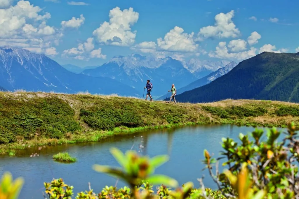 Zwei Wanderer auf einem Weg mit Bergpanorama und See im Vordergrund