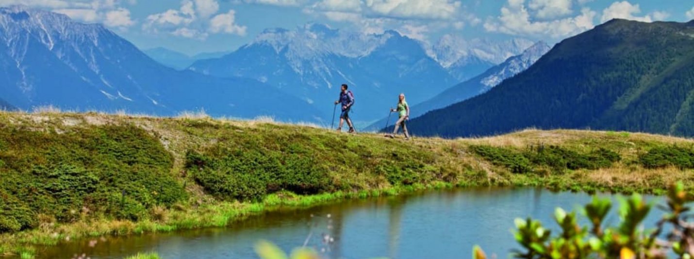 Aktivurlaub für Erlebnissammler - 5 Nächte Zwei Wanderer auf einem Weg mit Bergpanorama und See im Vordergrund