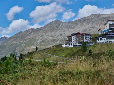 Alpenhotel am Hang mit Bergpanorama unter blauem Himmel