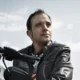 Man in leather jacket sitting on black motorcycle with helmet nearby