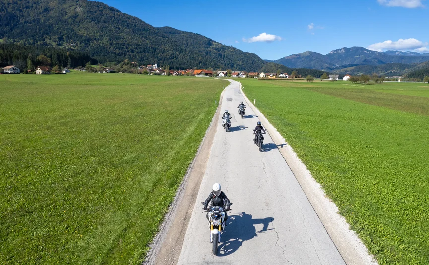 Four motorcyclists riding on a country road through green fields and mountains