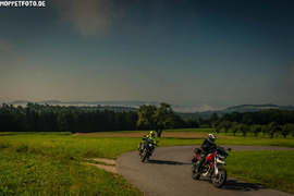 Zwei Motorräder fahren auf Landstraße in grüner Landschaft bei klarem Himmel