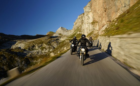 Drie motorfietsers rijden op bergweg onder heldere blauwe lucht