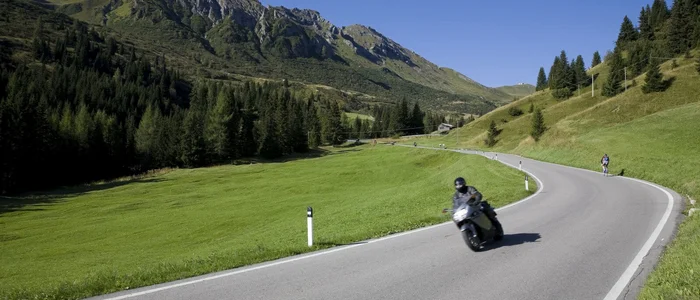 Motorcoureur op kronkelende bergweg met groene weiden en bergen