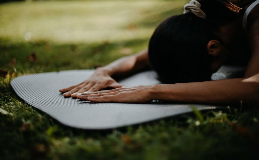 Vrouw die yogastretches doet op een mat buiten op gras