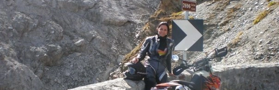 Motorradfahrerin in Lederkleidung an Bergstraße mit Kurvenschild auf 2696 m Höhe