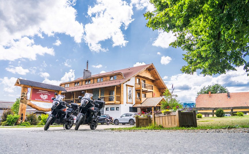 Motorräder vor einem Alpenhotel mit blauem Himmel und Bäumen