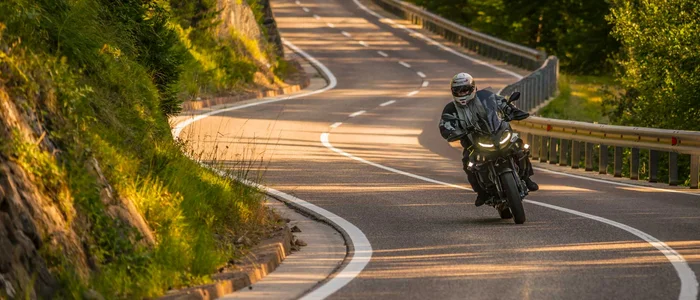Motorradfahrer auf kurviger Landstraße in sonniger Landschaft