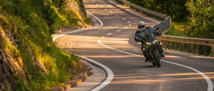 Motorradfahrer auf kurviger Landstraße in sonniger Landschaft
