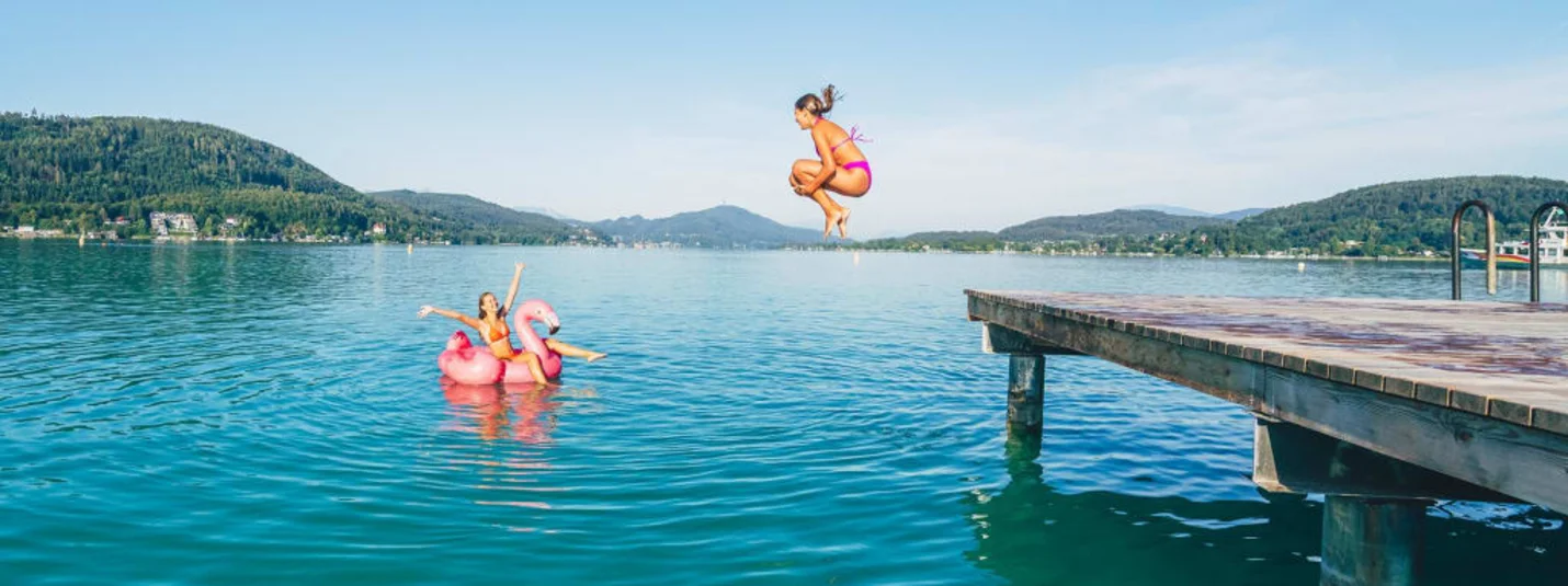 Summer sun, bathing fun Woman jumping off pier into lake, another on flamingo float