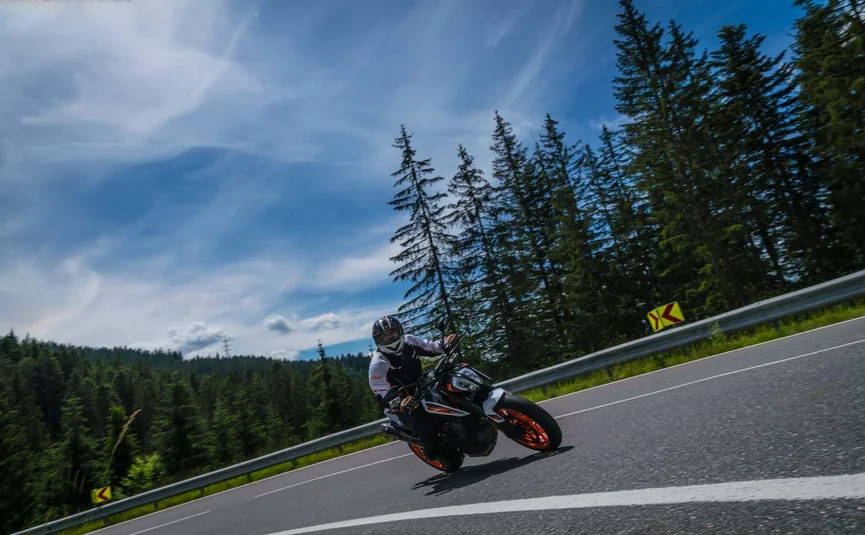 Motorcyclist riding on a winding road near forest under blue sky