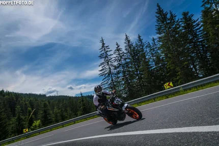 Motorcyclist riding on a winding road near forest under blue sky