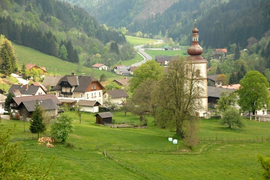 Dorf mit Kirche und grünen Hügeln in einer bergigen Landschaft