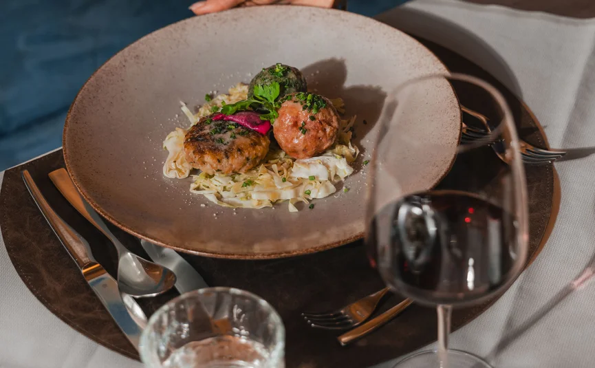 Hand serving plate with three meat patties and red wine on set table
