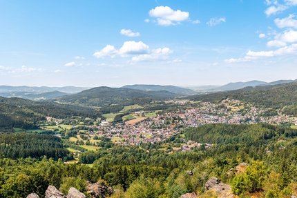 Panoramisch uitzicht op een stad in een vallei omringd door beboste heuvels en blauwe lucht