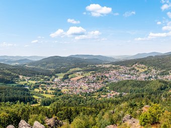 Panoramablick auf eine Stadt im Tal umgeben von bewaldeten Bergen und blauem Himmel