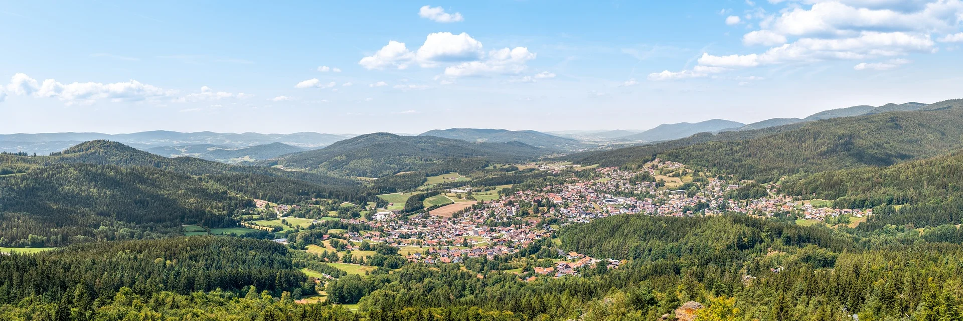 Panoramic view of a town in a valley surrounded by forested hills and blue sky