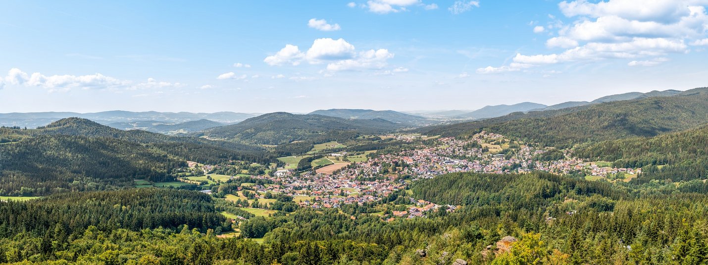 Motorradurlaub im Bayerischen Wald © Bodenmais Panoramablick auf eine Stadt im Tal umgeben von bewaldeten Bergen und blauem Himmel