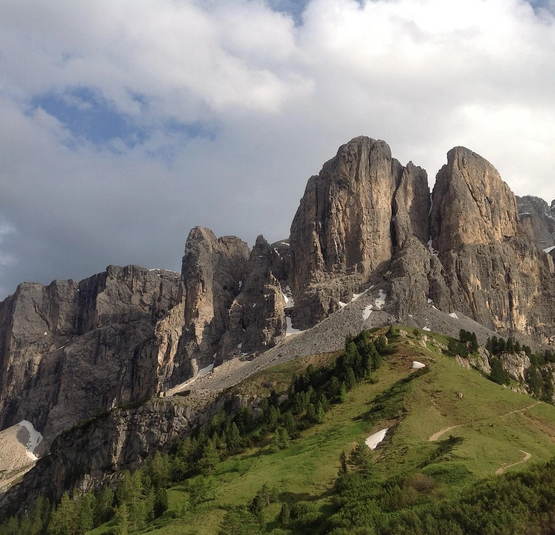 Felsige Bergspitze mit grünen Hängen und bewölktem Himmel