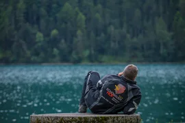 Man lying relaxed on stone bench facing lake and forest