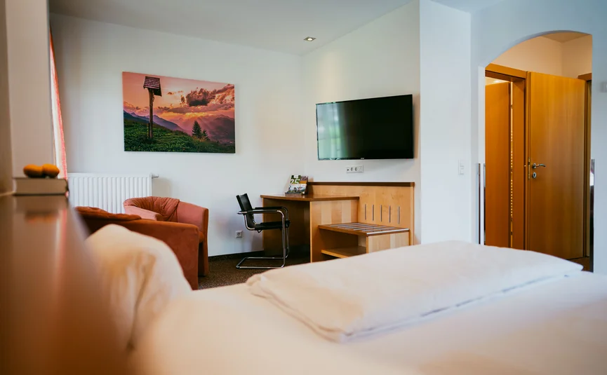 View of a bright hotel room with bed, TV, and seating area