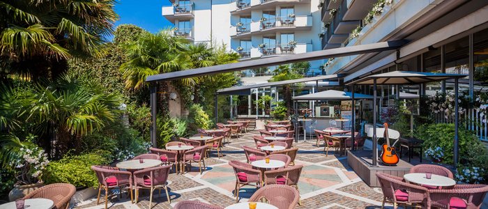 Outdoor café with pink chairs and small tables in front of a hotel building