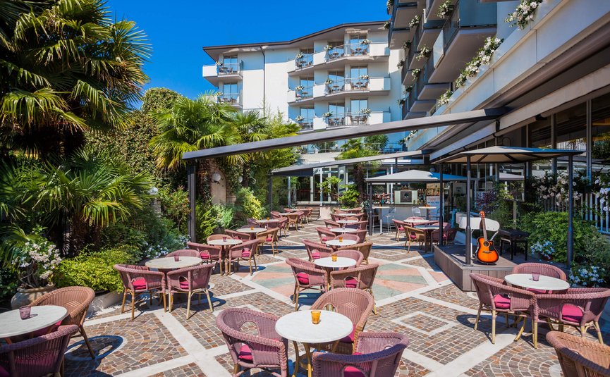 Outdoor café with pink chairs and small tables in front of a hotel building