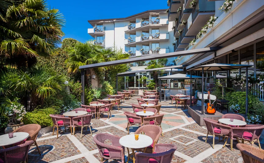 Freiluftcafé mit rosa Stühlen und kleinen Tischen vor einem Hotelgebäude