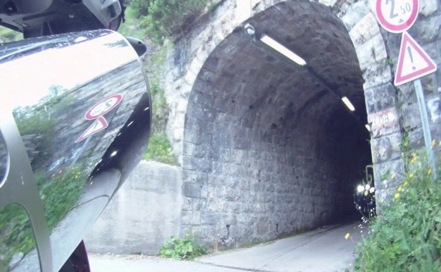 Motorrad vor einem dunklen Steintunnel mit Verkehrsschildern am Eingang