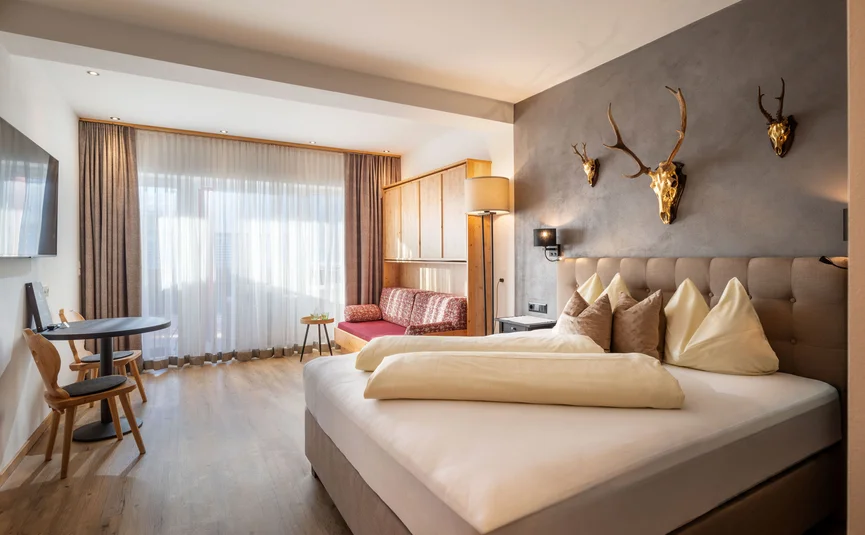 Modern hotel room with double bed, sofa, and decorative animal skulls on wall