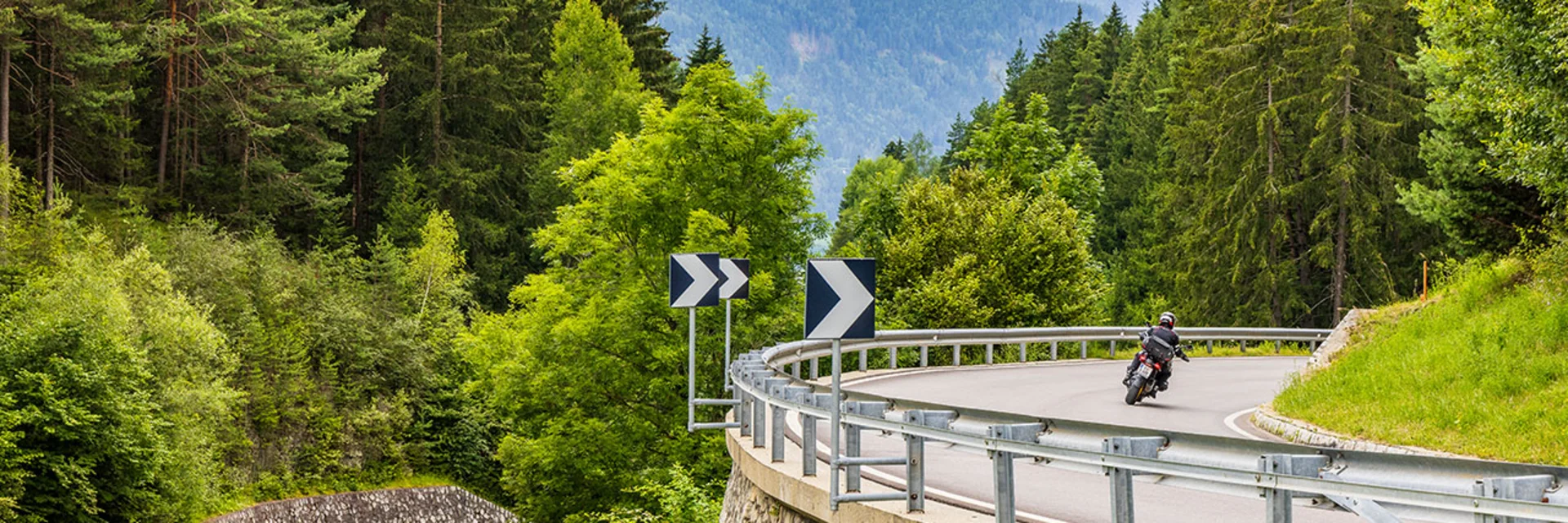 Motorcyclist riding on winding mountain road through forest