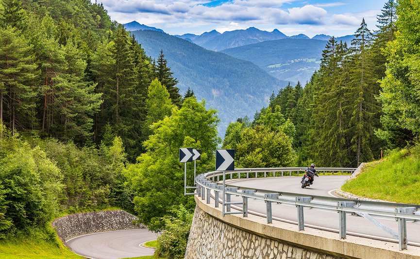 Motorradurlaub in Südtirol und den Dolomiten © Alexander Seger Motorradfahrer fährt auf kurviger Bergstraße im Wald