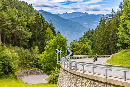 Motorradfahrer fährt auf kurviger Bergstraße im Wald