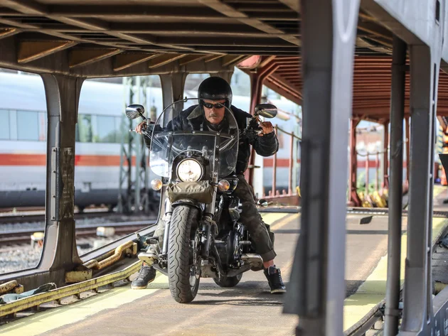 Mann auf Motorrad fährt auf Bahnverladung mit Zug im Hintergrund