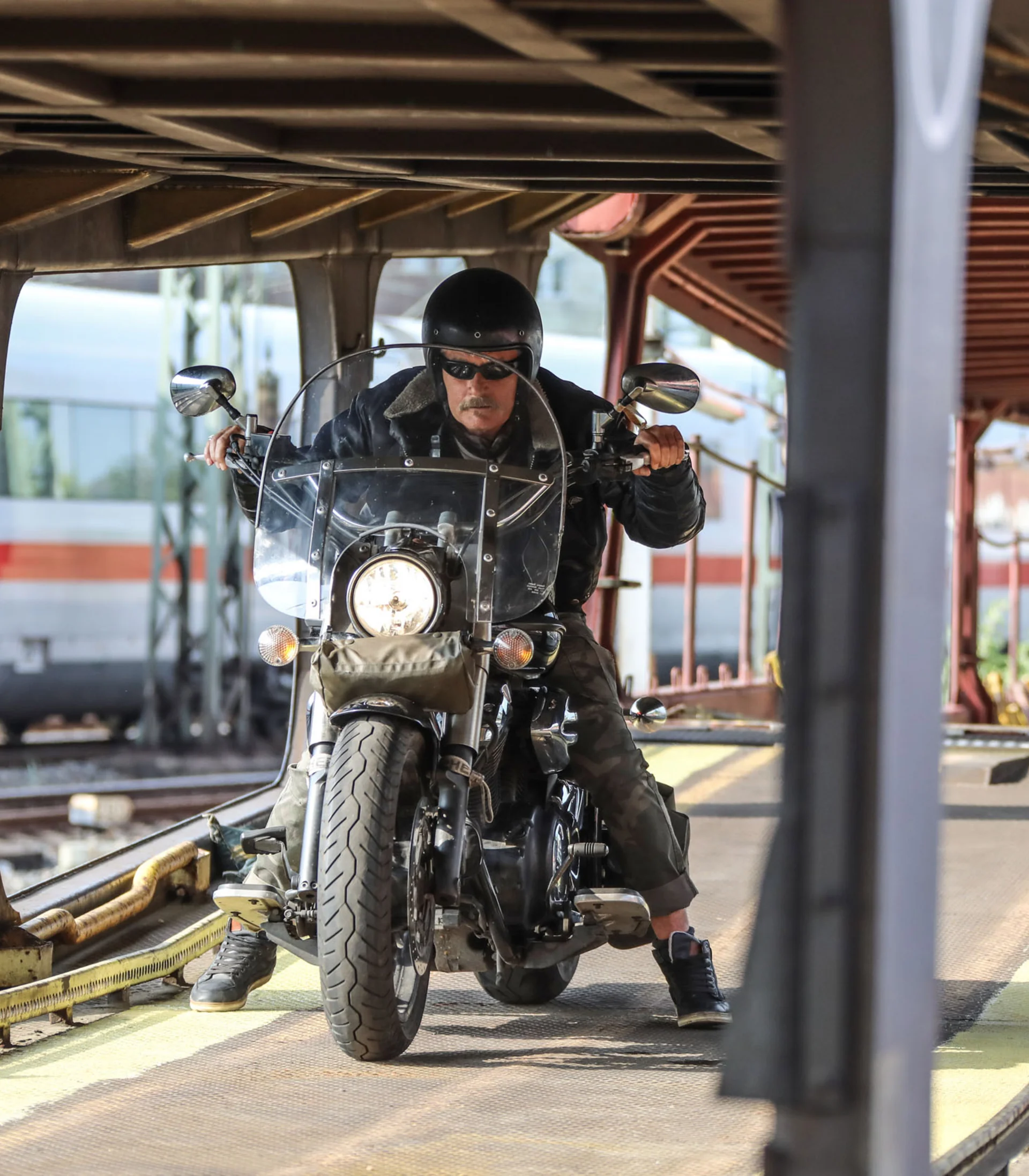 Man riding motorcycle on train loading ramp with train in background