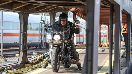 Mann auf Motorrad fährt auf Bahnverladung mit Zug im Hintergrund