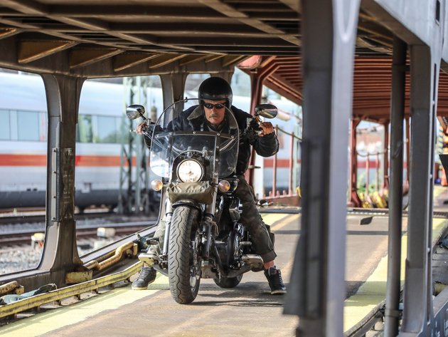 Motorrad- und Autoreisezug © Eduard Bopp Mann auf Motorrad fährt auf Bahnverladung mit Zug im Hintergrund