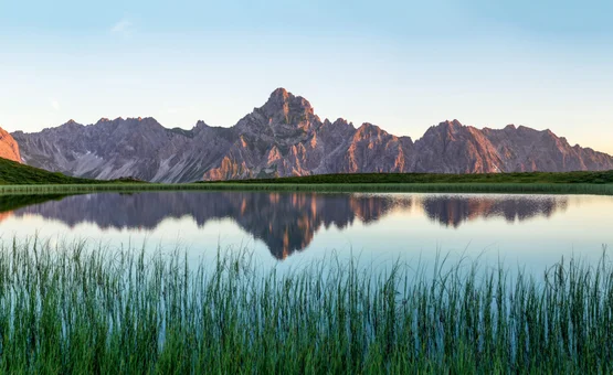 Bergspitzen spiegeln sich in einem ruhigen See umgeben von grünen Hügeln