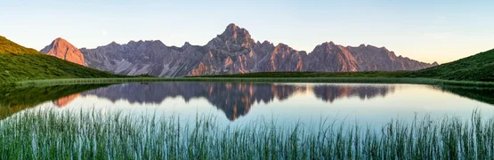 Mountain peaks reflecting in a calm lake surrounded by green hills