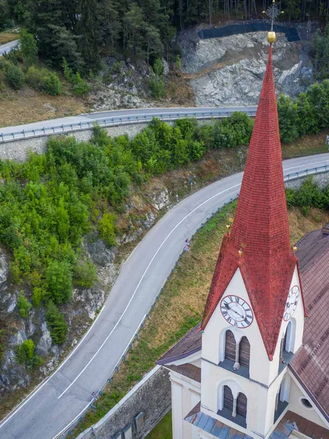 Church steeple with red roof by winding mountain road and forest