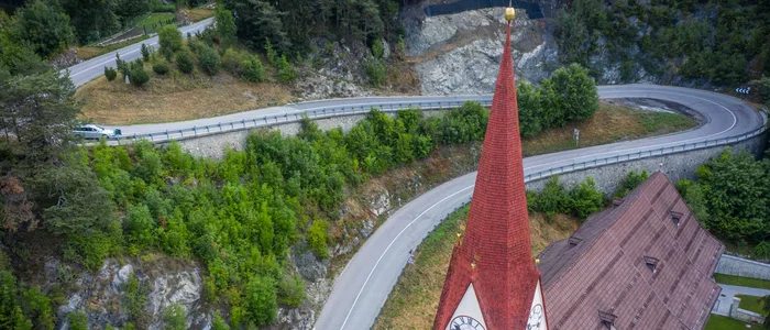 Church steeple with red roof by winding mountain road and forest
