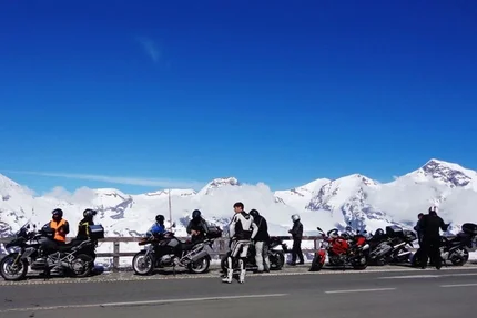 Motorcyclists with bikes on mountain road with snowy peaks