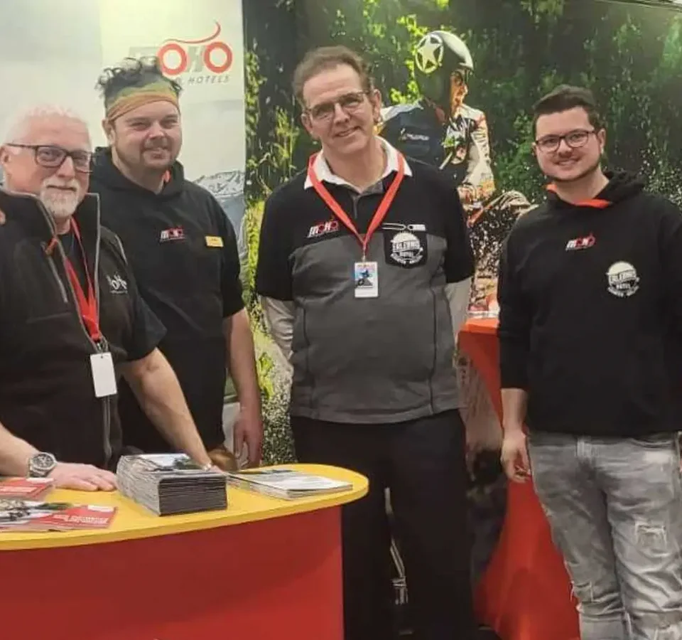 Vier mannen bij een Motorrad Hotels stand op een beurs